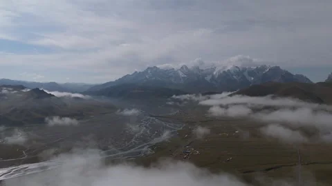 Aerial view above clouds over a mountain valley and snow peaks, Kyrgyzstan Stock Footage 347241259