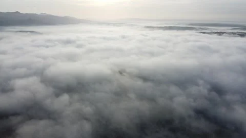 Aerial view above dense cloud layer over distant mountain ranges at sunrise Stock Footage 343235775