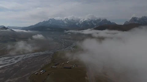 Aerial view above low clouds over a valley with snow peaks, Kyrgyzstan Stock Footage 347241272