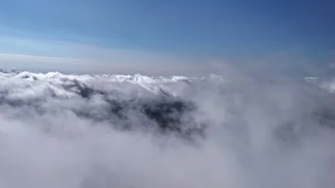 Aerial view above a thick cloud layer with blue sky overhead, revealing a Vidéo 334000293