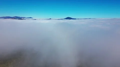 Aerial view above a vast rolling sea of clouds with distant silhouetted 스톡 동영상 345972623