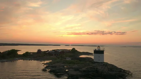 Aerial view of a active lighthouse &amp; cabins on a remote island during sunset Stock Footage 134918363