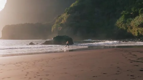 Aerial view of active young man running on black beach at sunrise Stock Footage 299960483