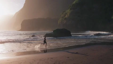Aerial view of active young man running on black sand volcanic at sunrise Stock Footage 299960492