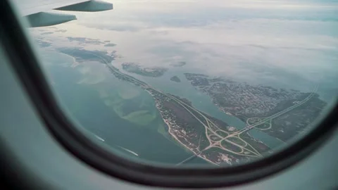 Aerial view from airplane window capturing coastal landscape with winding roads, Video stock 329201750
