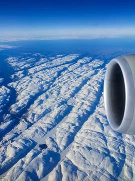 Aerial view from an airplane window featuring a jet engine above a vast snow-cov Stock Photos