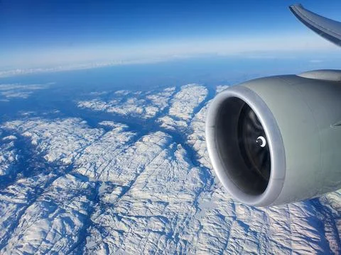 Aerial view from an airplane window featuring a jet engine above a vast snow-cov Stock Photos