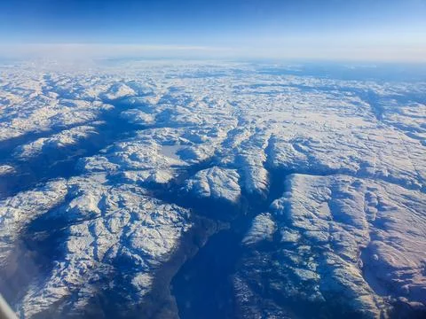 Aerial view from an airplane window featuring a jet engine above a vast snow-cov Stock Photos
