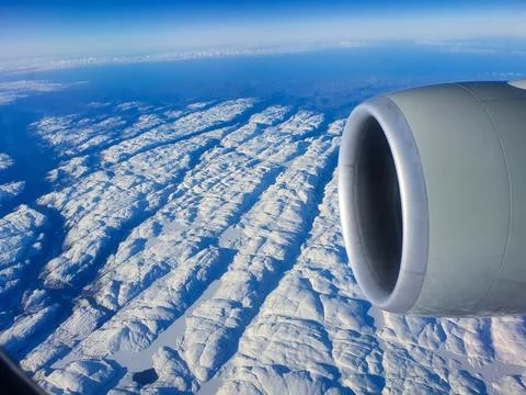 Aerial view from an airplane window featuring a jet engine above a vast snow-cov Stock Photos