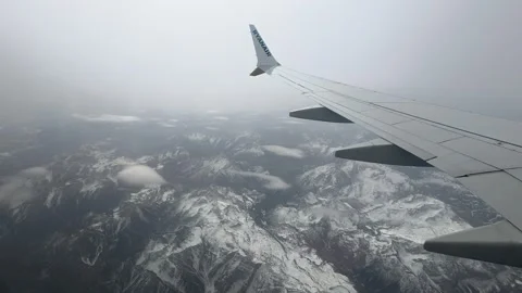 Aerial View from Airplane Window Over Snow-Covered Mountain Range in Winter Видео 335954465