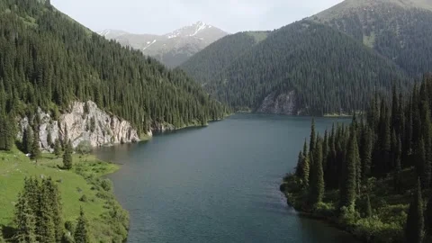 Aerial view of alpine lake with forest and snow-capped peaks at Kolsay Lakes Stock Footage 345410378