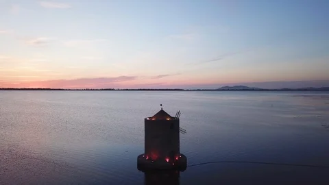 Aerial View around An ancient romantic windmill on a sea lagoon at orange dusk Stock Footage 107848051