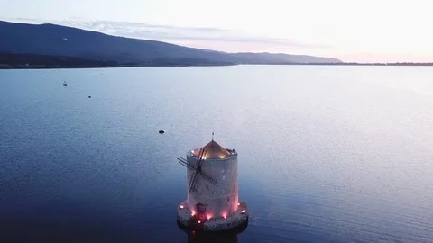 Aerial View around An ancient romantic windmill on a sea lagoon at dusk Stock Footage 107848114