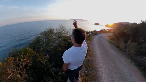 Aerial view around a man standing on a scenic path on the cliff at sunset, Stock Footage 107968066