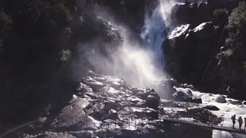 Aerial view - Backlight alpine waterfalls with a bridge over it and trekkers Stock Footage 137349375