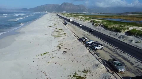 Aerial view of a beach with waves, a road with cars, and mountains in the Stock Footage 308976804
