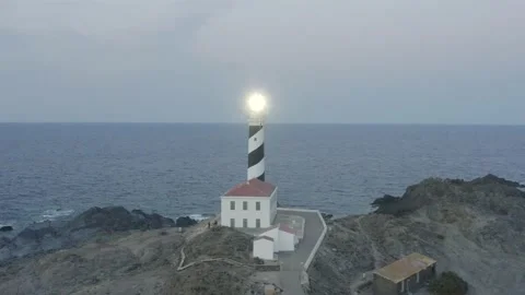 Aerial View Of Beautiful Shining Lighthouse On Rocky Cliff Just After Sunset Stock Footage 136560045
