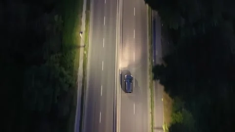 Aerial view of a black car driving on a well-lit road at night 库存影片 337929894