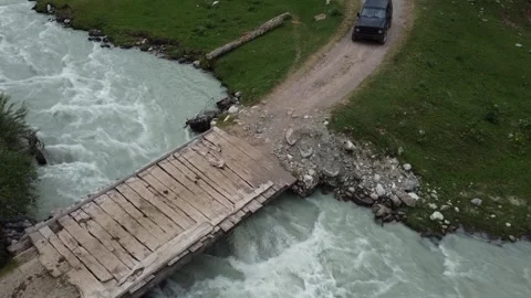 Aerial View of Black SUV Approaching Old Wooden Bridge over Rushing River Video stock 332204998