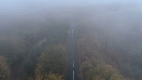Aerial view of black SUV with turned headlights driving along spooky foggy road Stock Footage 119310710
