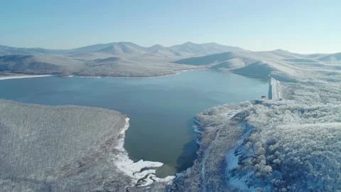 Aerial view on a blue lake between the snowy mountains and iced frozen forest Stock Footage 153685334