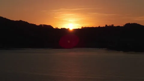 Aerial view of bright sun emerging from behind mountain hill over lake water Видео 345606754