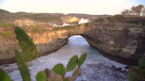 Aerial view of a broken beach with a cliff, waterfall, and rock arches in Bali. Stock Footage 273144666