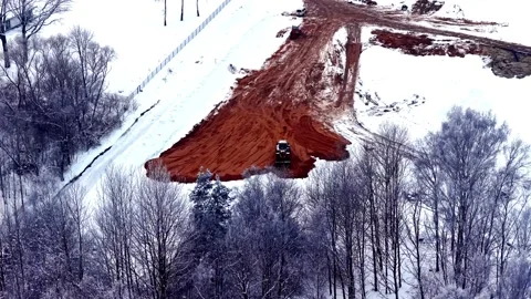 Aerial view of bulldozer working on red soil patch in snowy winter landscape in Video stock 327517871