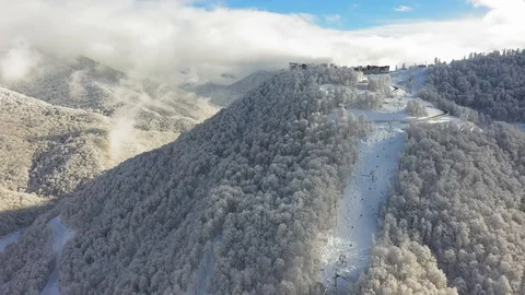 Aerial view. Cabins of ropeway move by snowy mountain slope at winter sunny day. Vidéo 100392856