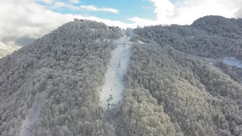 Aerial view. Cabins of ropeway move by snowy mountain slope at winter sunny day. Vidéo 100392928