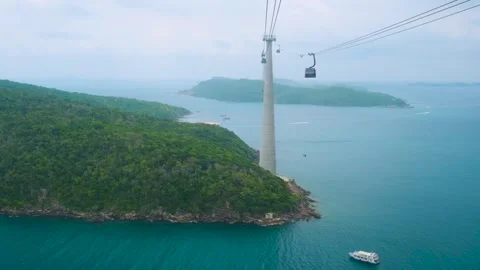 Aerial view of cable car gondola gliding over lush green island hills and Stock Footage 312814101