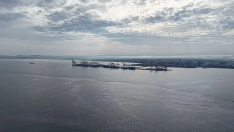 Aerial view of calm sea with cloudy sky and distant industrial harbor Stock Footage 336947769