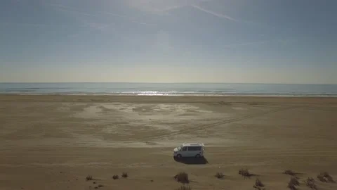 Aerial view of a camper van driving along a sandy beach on a summer day Stock Footage 159440150