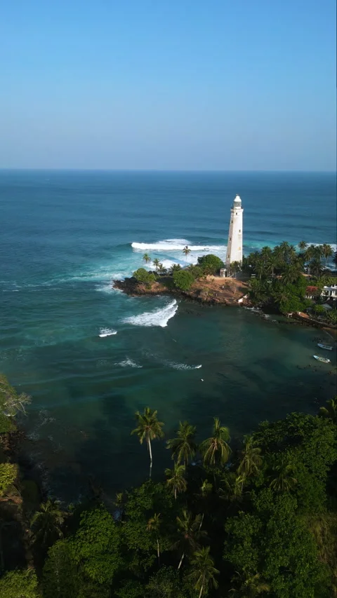 Aerial view captures a historic lighthouse, surrounded by tropical palms and a Stock Footage 265166226