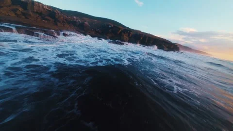 Aerial view captures ocean waves hitting jagged rocks during golden hour Stock Footage 340914901