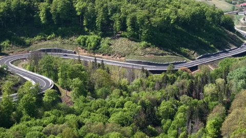 An aerial view captures a winding highway cutting through a dense green forest Stockbeeldmateriaal 334138738