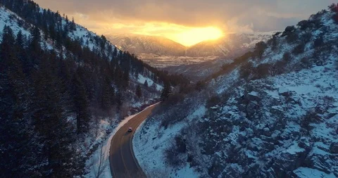 Aerial view car driving down snow covered winter road in canyon at sunset Stock Footage 86325986