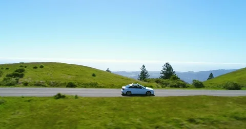 Aerial view of car driving down country road through rural grassy hills Stock Footage 89149355