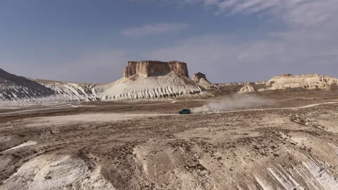 Aerial view of a car driving through an expansive desert canyon of Bozjyra or Stock Footage 322047992