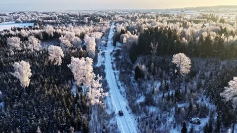 Aerial view of a car driving through a snowy forest road Stock Footage 332455444