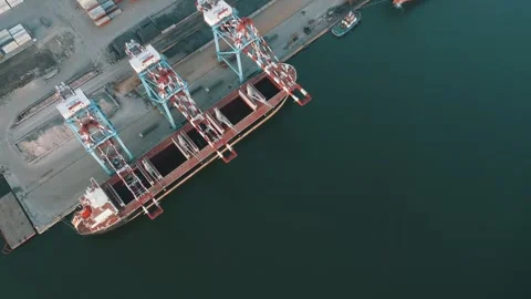 Aerial view of a cargo ship docked at an industrial port with cranes unloading Stock Footage 311184489