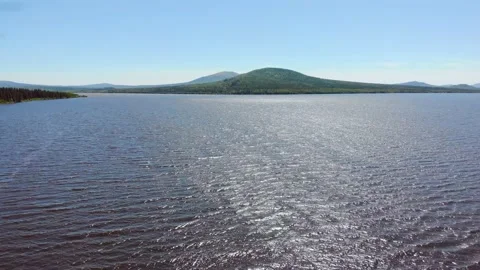 Aerial view of clear deep blue lake. Thick lush trees grow on the banks. Light Stock Footage 156190381
