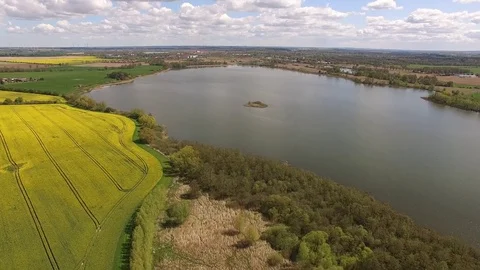 Aerial view of colorful rape fields with a lake under blue sky in germany Stock Footage