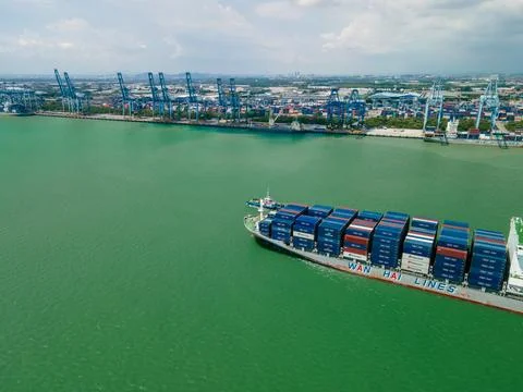 Aerial view of container ship sailing near a busy cargo port. 库存照片