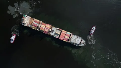 Aerial view of a container ship is seen assisted by two tugboats as it departs Stock Footage 252021423