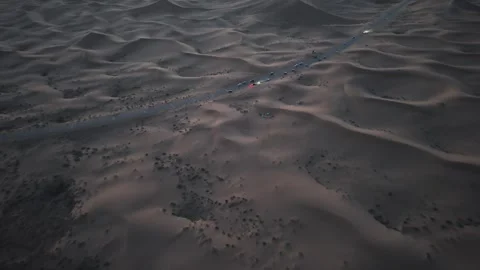 Aerial view of convoy driving through Tengger Desert dunes at dusk Stock Footage 345369879