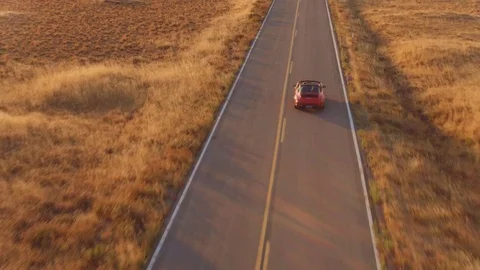 Aerial View Of Couple Driving Convertible Sports Car Down Country Road At Sunset Stock Footage