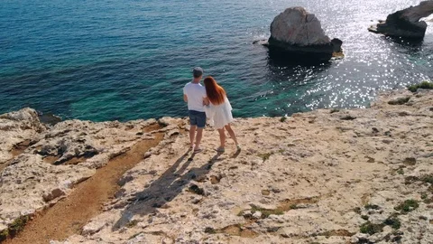 Aerial view of couple standing on edge of cliff by sea Stock Footage 107320745