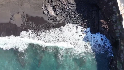 Aerial view of crashing ocean waves on a black sand beach with people walking Видео 335877216