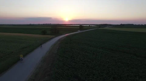 Aerial view of cyclist rides between fields at sunset Stock Footage 50997120